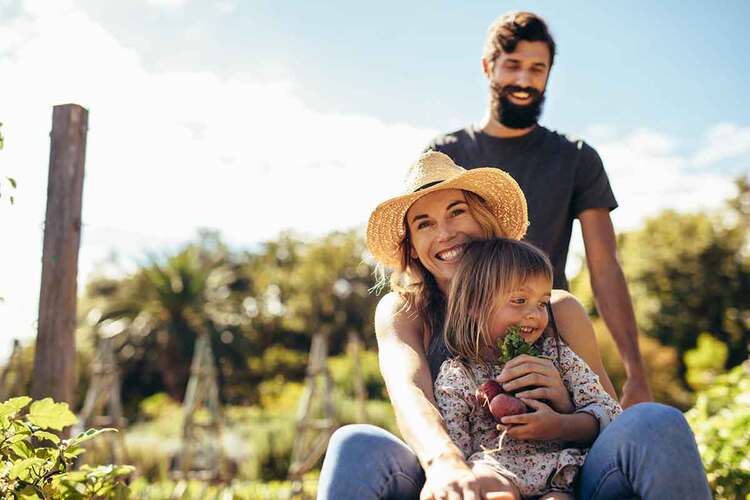 Young man gives his woman and daughter ride in wheelbarrow. Happy family a ride in wheelbarrow at farm.